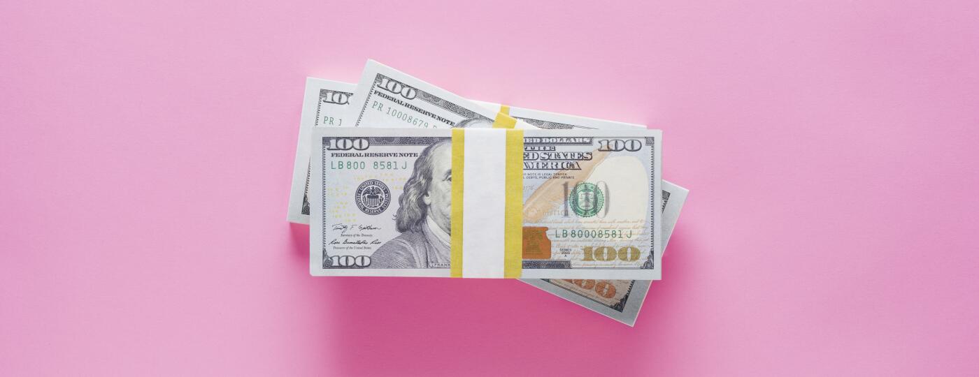 stacks of 100 dollar bills on pink background