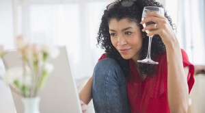 Mixed race woman drinking wine and using laptop