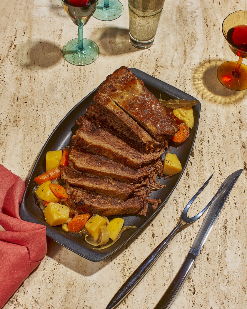 Sliced pot roast on a black platter served with red wine