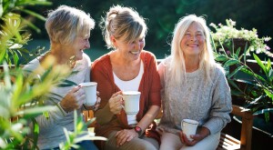 Three middle-aged women on bench with coffee, talking and laughing