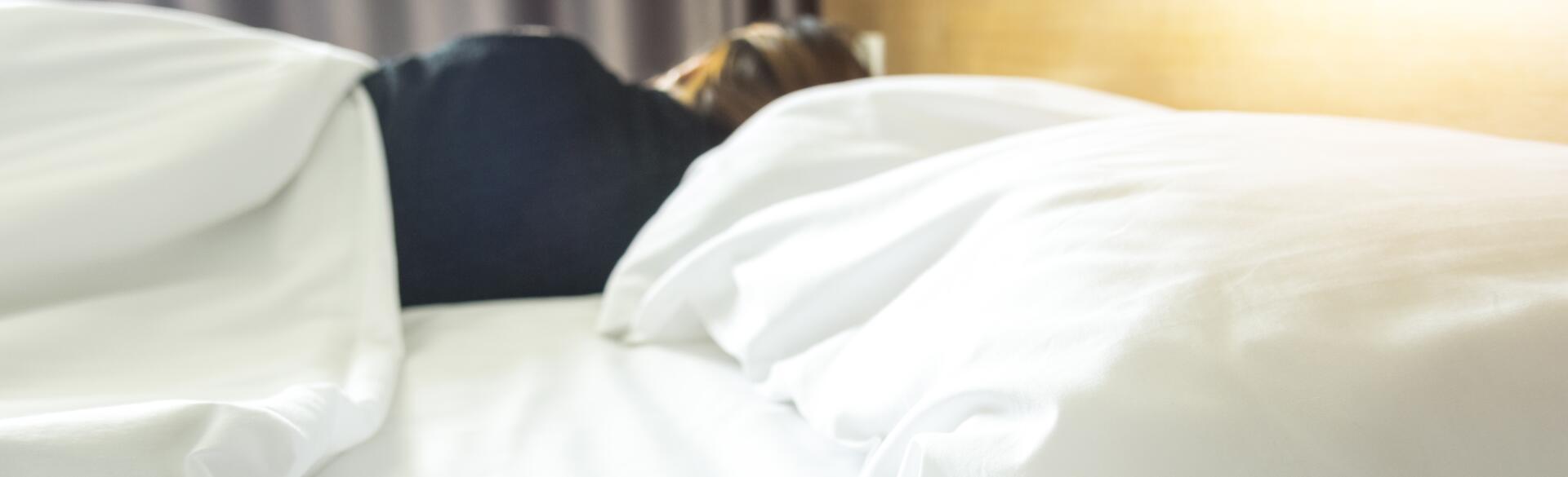 Woman sleeping on the far side of a bed with an empty pillow