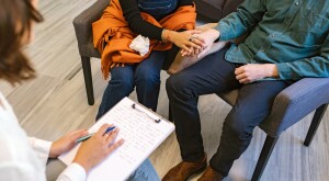 Couple holding hands talking to a therapist with a clip board
