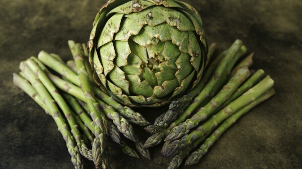 A still life of an aritchoke and asparagus on a textured background