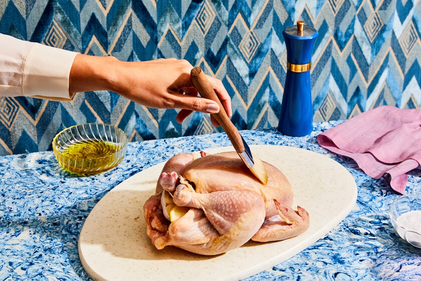 Hand brushing raw chicken with olive oil