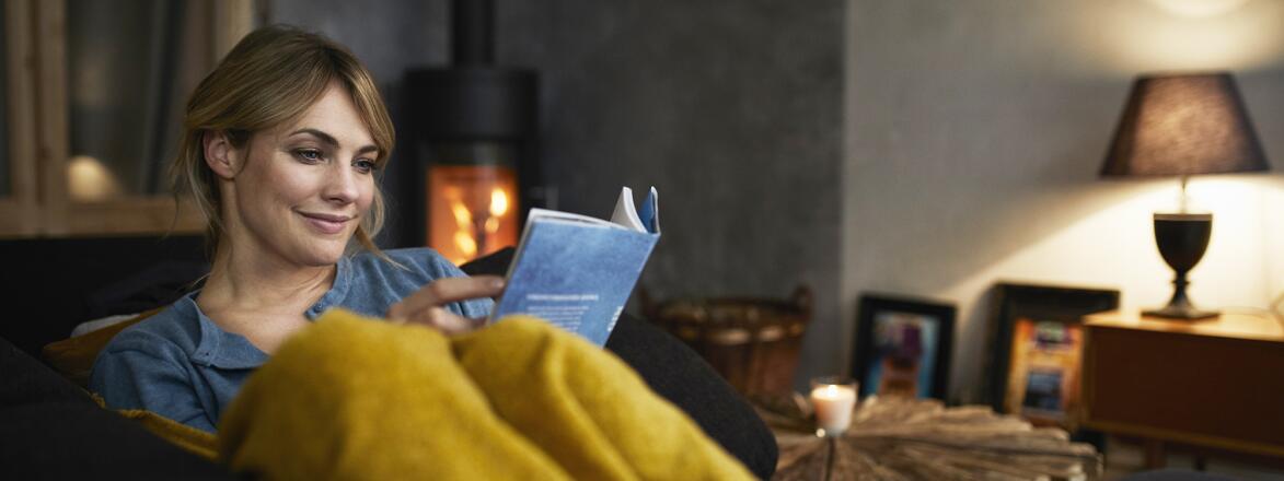 Woman reading book on couch in front of fireplace