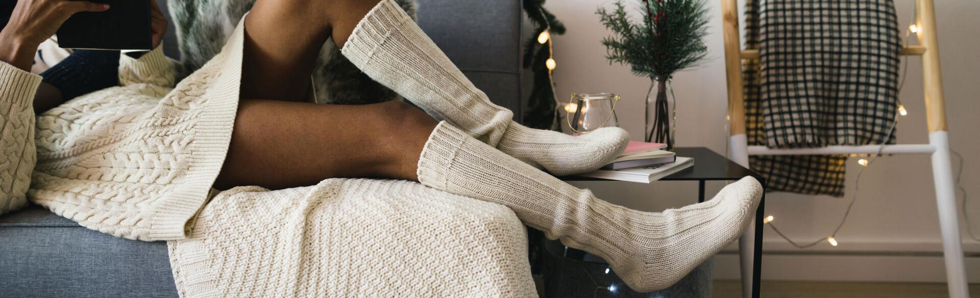 Woman lounging on a couch with Christmas lights in comfortable clothing reading a tablet