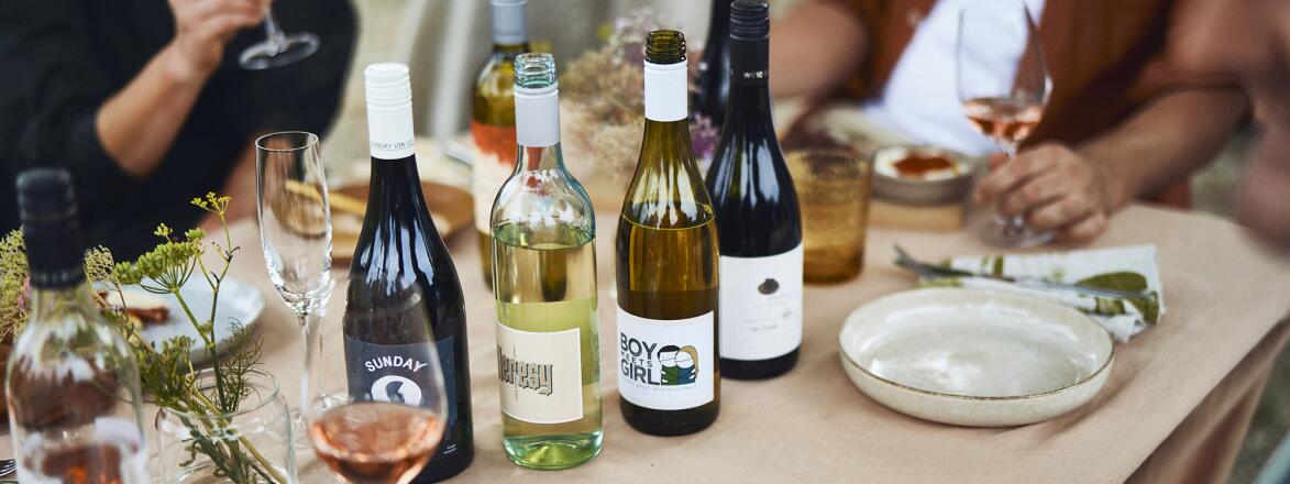Numerous people sitting around an outdoor set table with bottles of wines