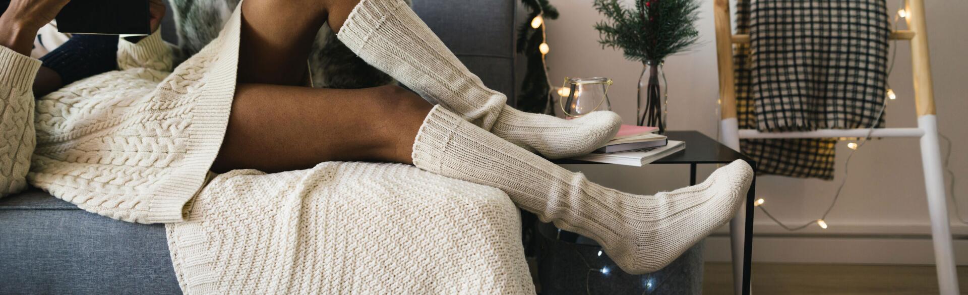 Woman lounging on a couch with Christmas lights in comfortable clothing reading a tablet