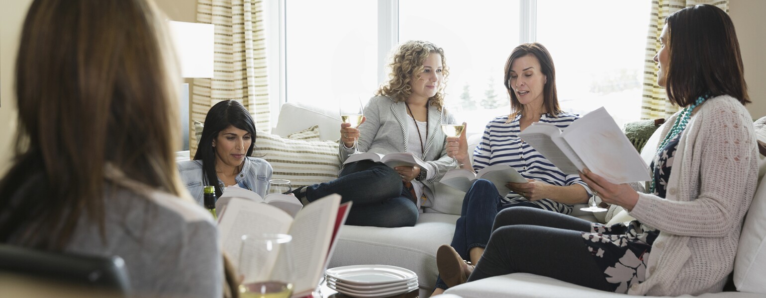 Mature female friends with wine glasses and books at a book club