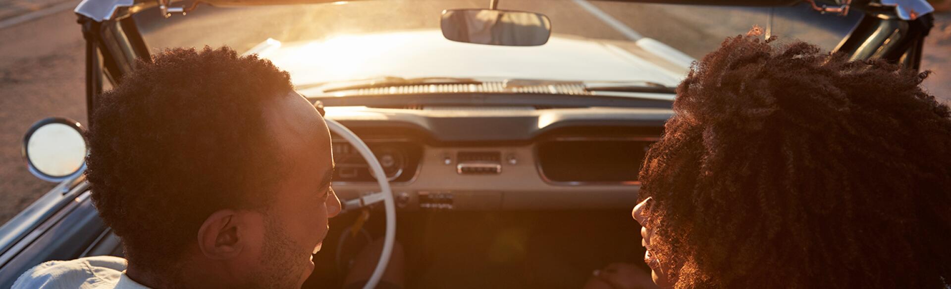 husband and wife in convertible driving into the sunset talking to each other