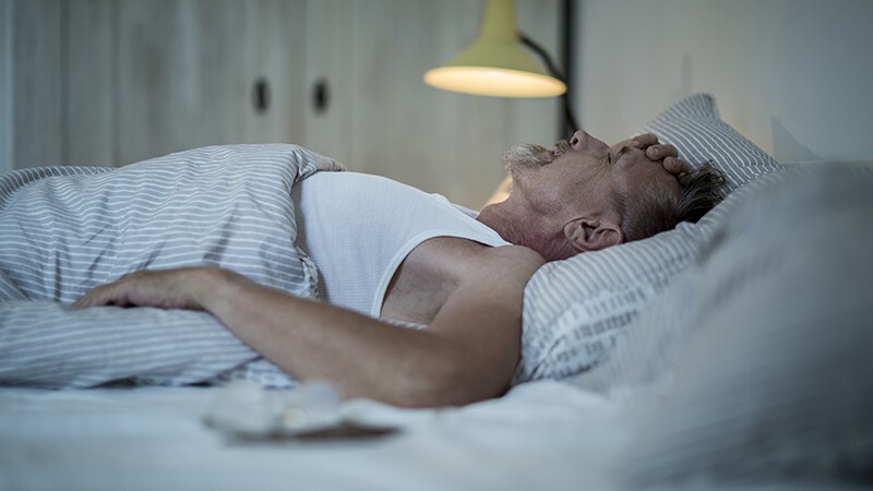 A man appearing stressed as he sleeps in bed