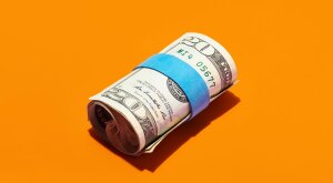 Money wrapped in a rubber band on an orange background
