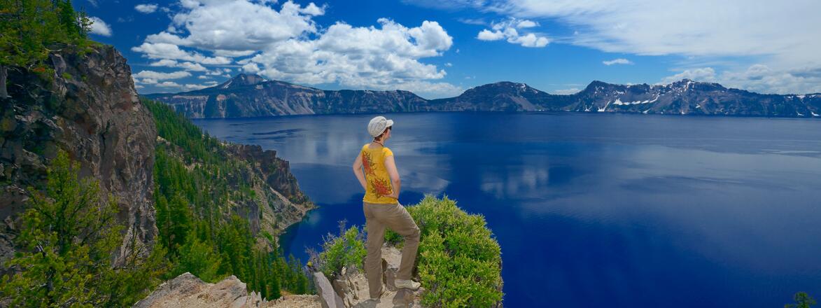 Woman with hat standing on rock, overlooking the lake at Crater Lake National Park, Oregon.