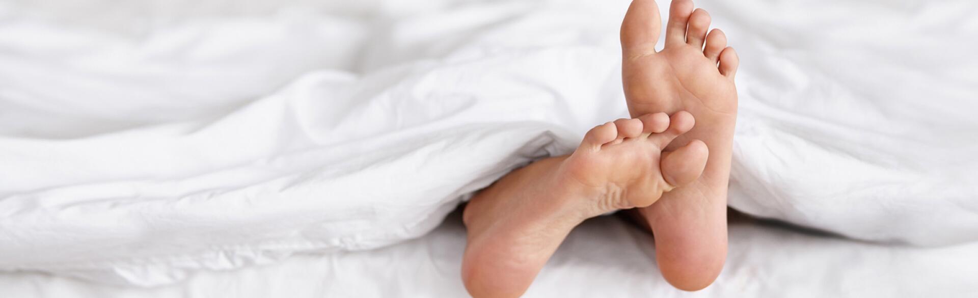 An image depicting two feet sticking out from underneath a white blanket in bed.