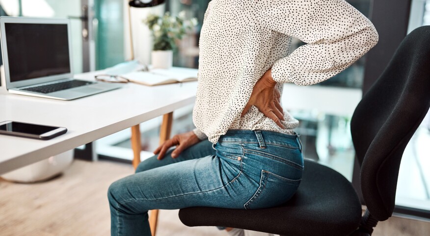 woman holding her aching back while sitting at her desk