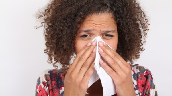 African-American woman sneezing into tissue