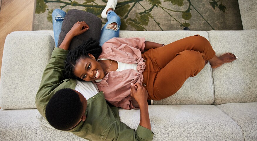 Young woman smiling at her boyfriend while lying on his lap on their sofa