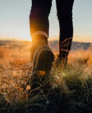 Women's boots walking through a field with the sun coming up 