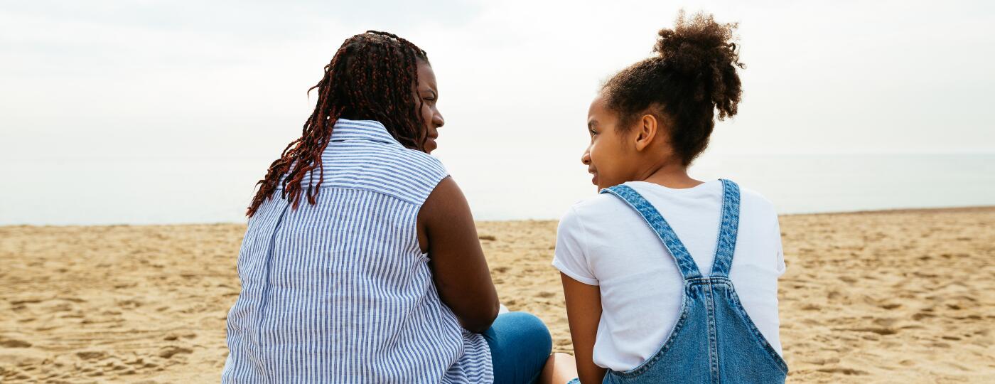 A stepmother sits with her stepdaughter on the beach.