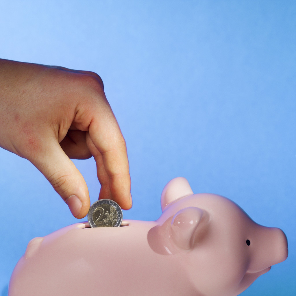 Close-up of human hand inserting two euro coin into piggy bank