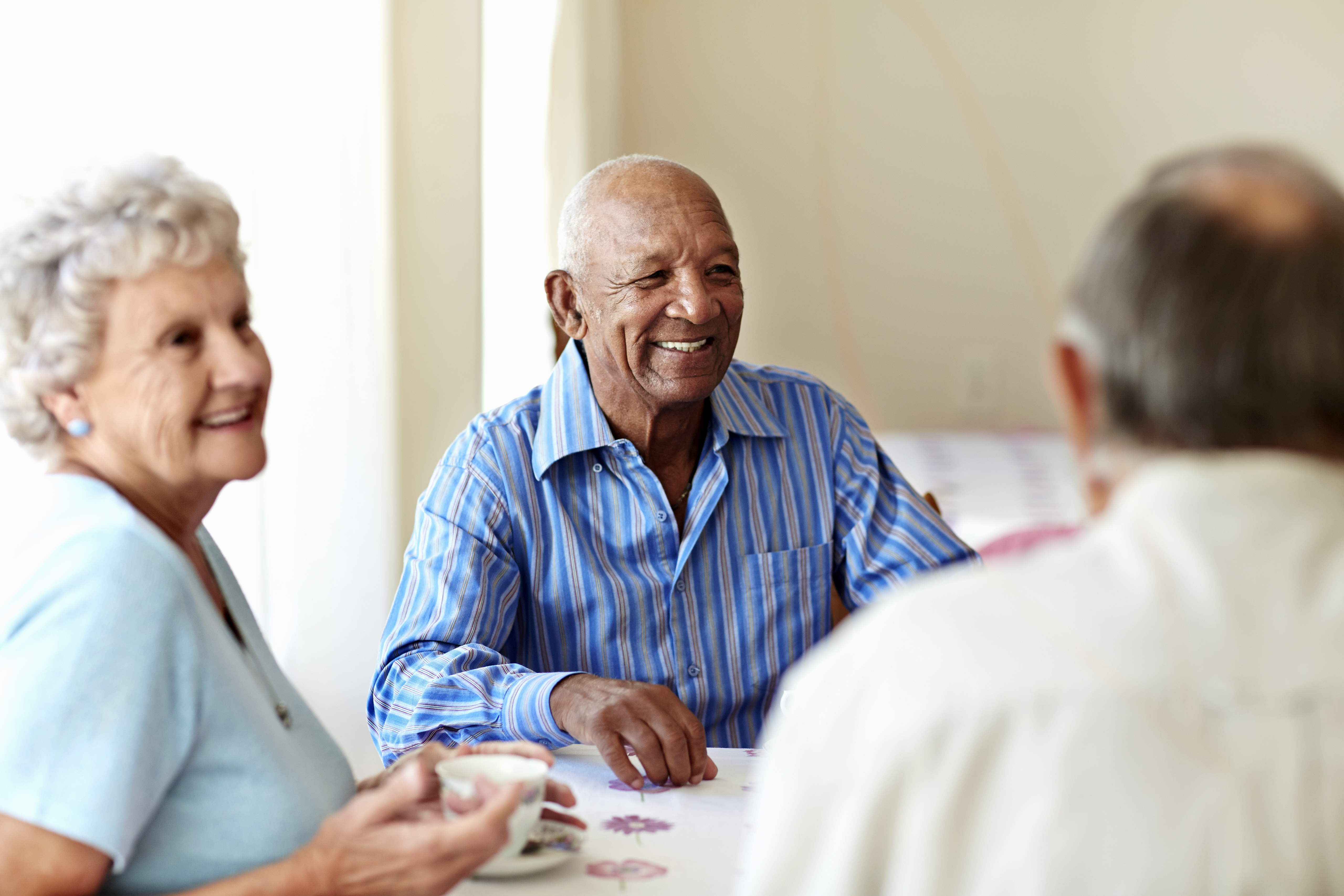 Happy senior man having coffee with friends at table in nursing home